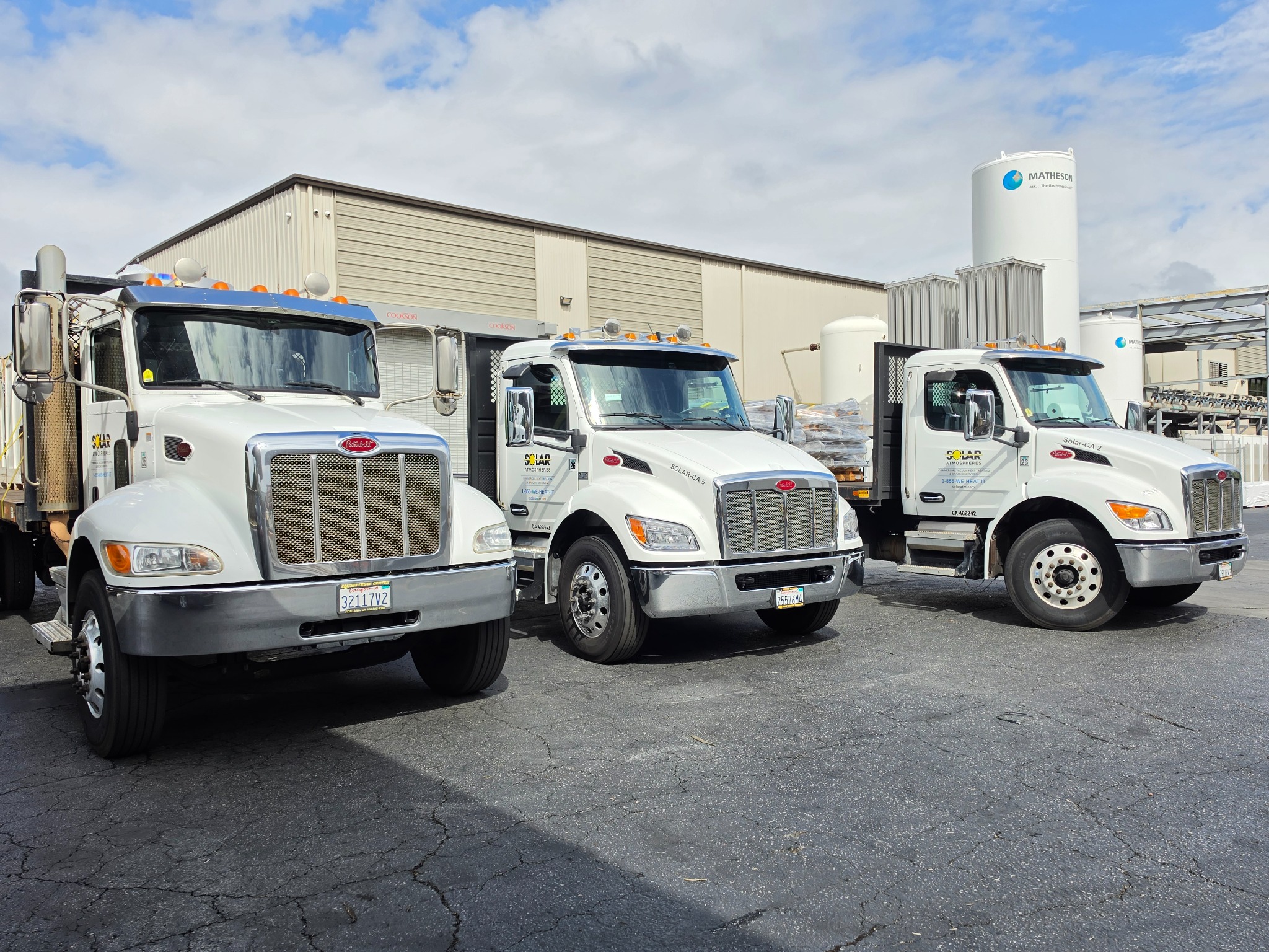 Three clean white commercial fleet truck cabs parked at an industrial facility.
